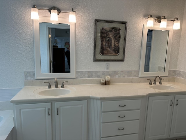 bathroom featuring double vanity, a textured wall, a bathtub, and a sink