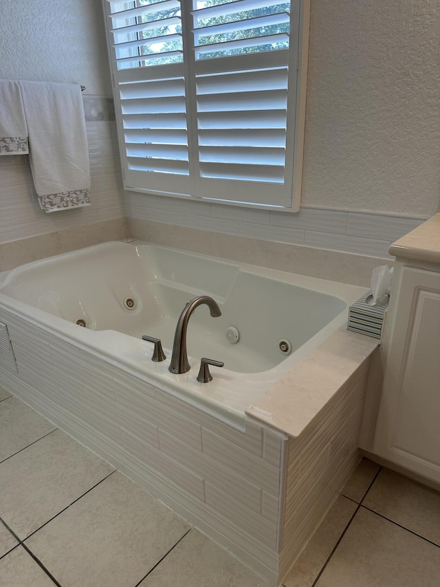 full bath featuring tile patterned floors, a tub with jets, and a textured wall