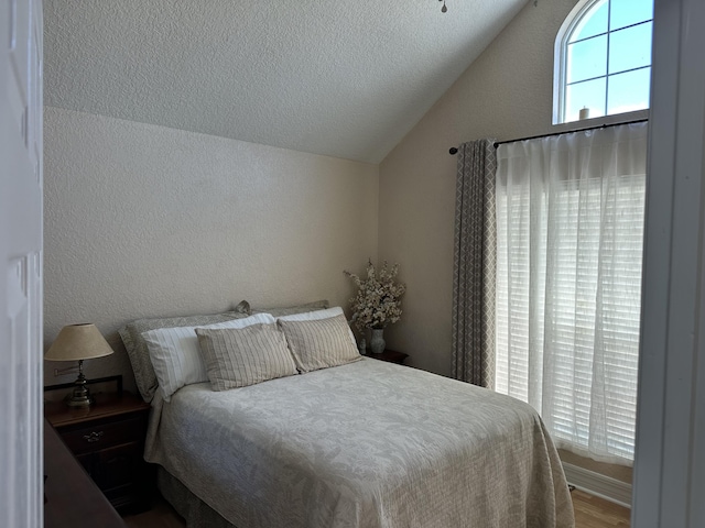 bedroom with lofted ceiling, a textured ceiling, and a textured wall