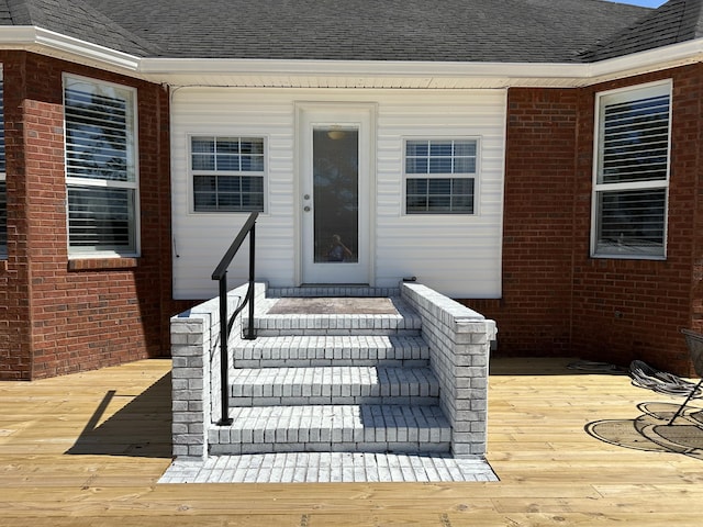 doorway to property featuring a deck, brick siding, and a shingled roof