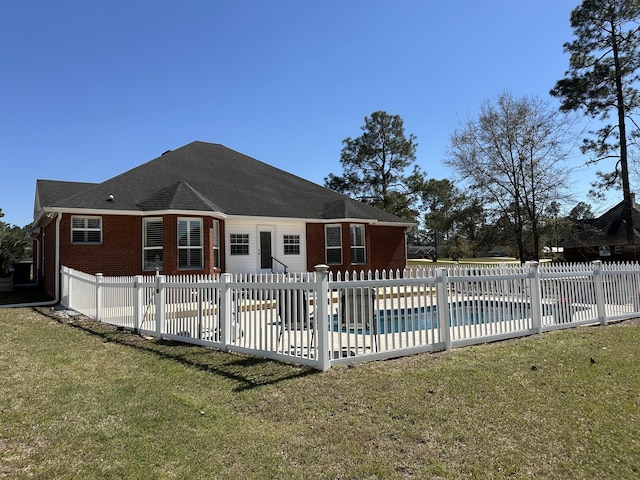 rear view of property featuring a fenced in pool, fence, roof with shingles, a lawn, and a patio