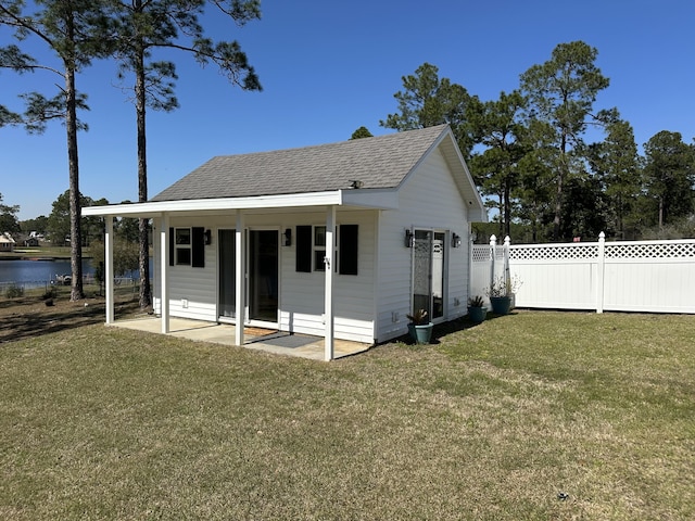 exterior space with a water view, a lawn, a patio, fence, and a shingled roof