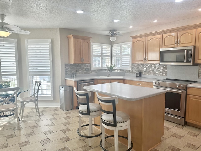 kitchen with light countertops, a ceiling fan, appliances with stainless steel finishes, and a center island