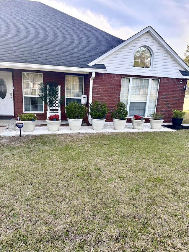 view of front of property featuring a front lawn, brick siding, and roof with shingles