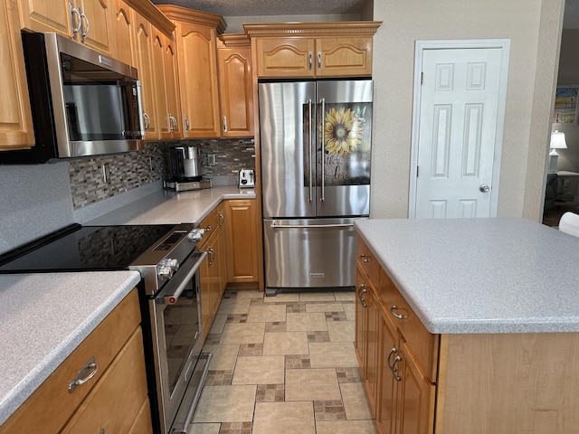 kitchen with brown cabinetry, a kitchen island, light countertops, appliances with stainless steel finishes, and tasteful backsplash