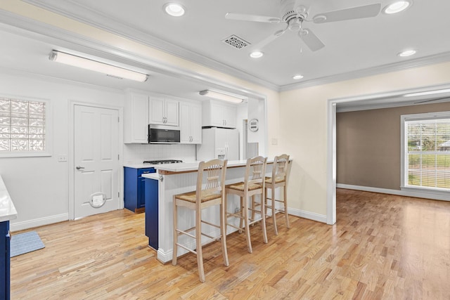 kitchen featuring crown molding, a breakfast bar area, stainless steel microwave, visible vents, and white fridge with ice dispenser