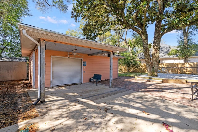 view of patio featuring a detached garage, a ceiling fan, fence, an outdoor structure, and driveway