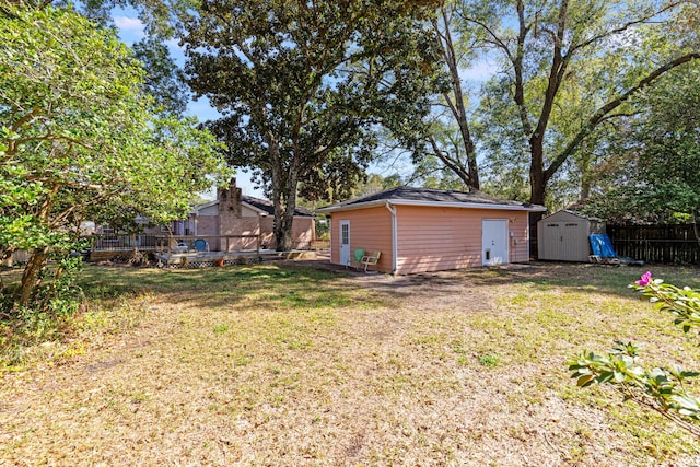 view of yard with a wooden deck, fence, a storage unit, and an outdoor structure