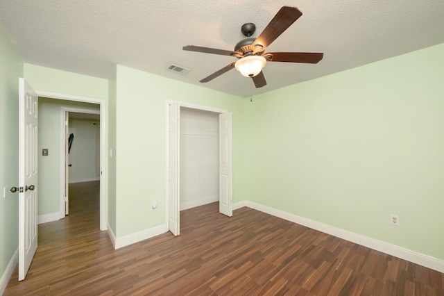 unfurnished bedroom featuring dark wood-style floors, a closet, visible vents, a textured ceiling, and baseboards