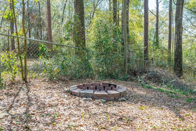 view of yard featuring a fire pit, a forest view, and fence