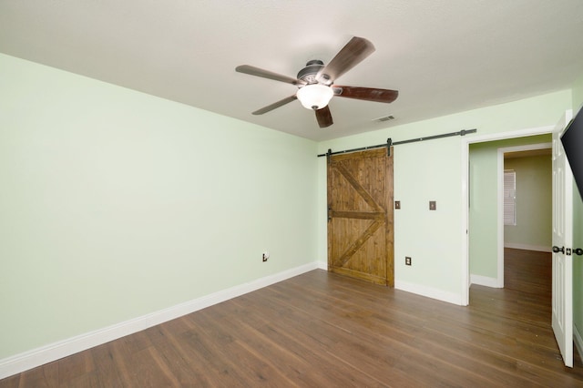 unfurnished bedroom featuring a barn door, visible vents, baseboards, ceiling fan, and dark wood-type flooring