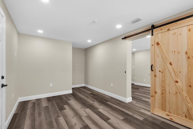 basement featuring a barn door, dark wood finished floors, visible vents, and baseboards