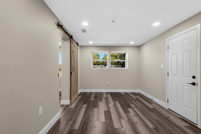 spare room featuring dark wood-type flooring, visible vents, baseboards, and a barn door