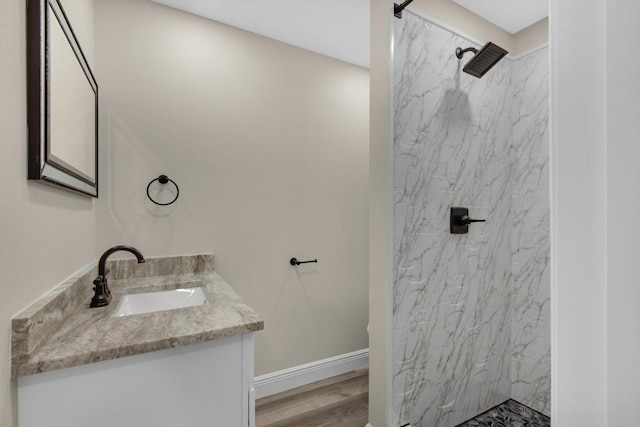 bathroom featuring wood finished floors, walk in shower, vanity, and baseboards