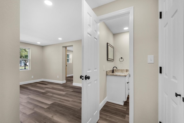 corridor featuring baseboards, dark wood-style flooring, a sink, and recessed lighting