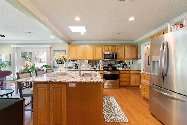 kitchen with ornamental molding, light wood-type flooring, appliances with stainless steel finishes, and a sink