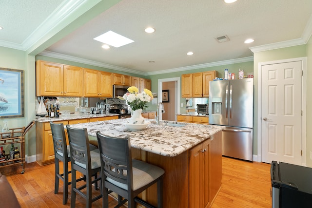 kitchen featuring a sink, stainless steel appliances, light wood-style floors, a breakfast bar area, and light stone countertops