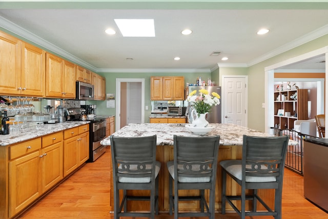 kitchen featuring a breakfast bar, ornamental molding, a kitchen island, light wood-style floors, and appliances with stainless steel finishes