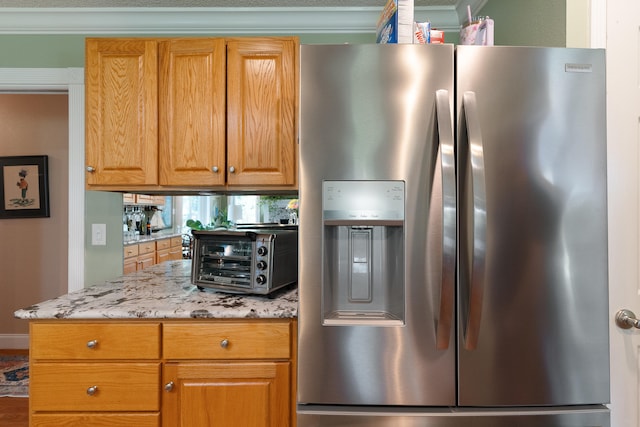 kitchen featuring light stone counters, a toaster, brown cabinetry, and stainless steel fridge with ice dispenser