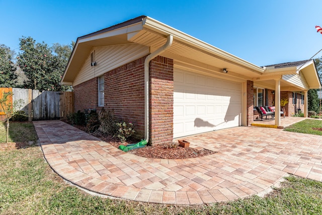 view of home's exterior featuring brick siding, an attached garage, driveway, and fence