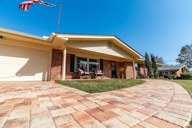 view of front of house featuring brick siding, an attached garage, a front yard, covered porch, and driveway