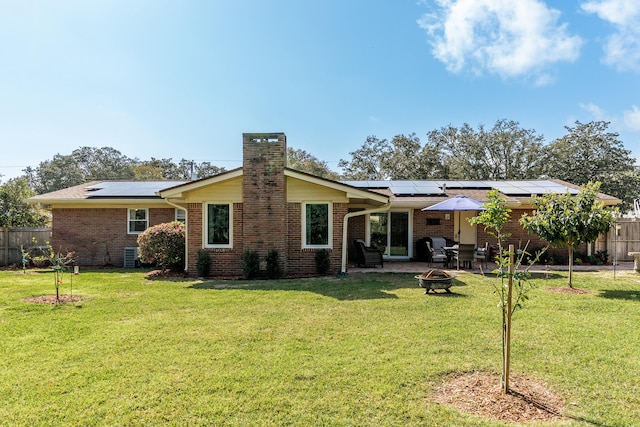 rear view of property featuring fence, brick siding, a lawn, and an outdoor fire pit