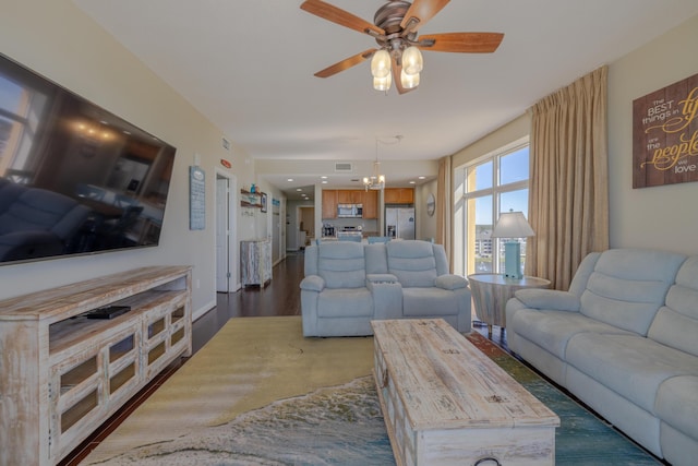 living area featuring baseboards, visible vents, dark wood-type flooring, and ceiling fan with notable chandelier