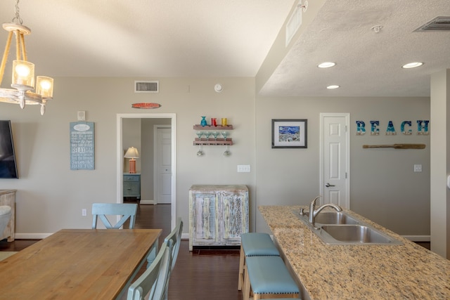 kitchen featuring dark wood-style floors, visible vents, hanging light fixtures, a sink, and baseboards