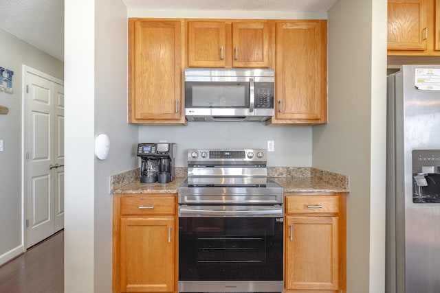 kitchen featuring stainless steel appliances, wood finished floors, and light stone countertops