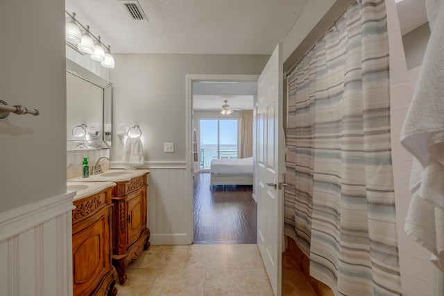 ensuite bathroom featuring visible vents, wainscoting, connected bathroom, a sink, and a textured ceiling