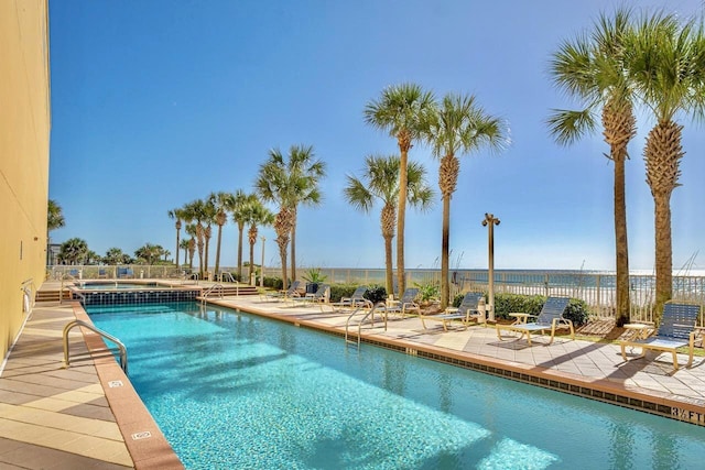 community pool with a patio area, fence, and a water view