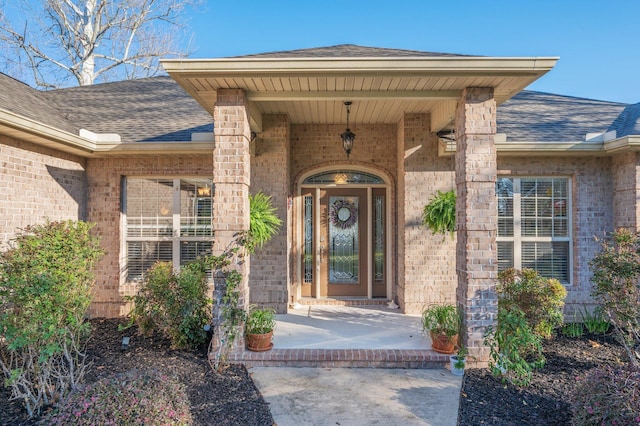 entrance to property featuring brick siding and a shingled roof