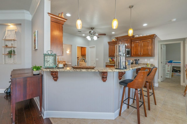 kitchen featuring light stone countertops, a breakfast bar area, hanging light fixtures, a peninsula, and brown cabinetry