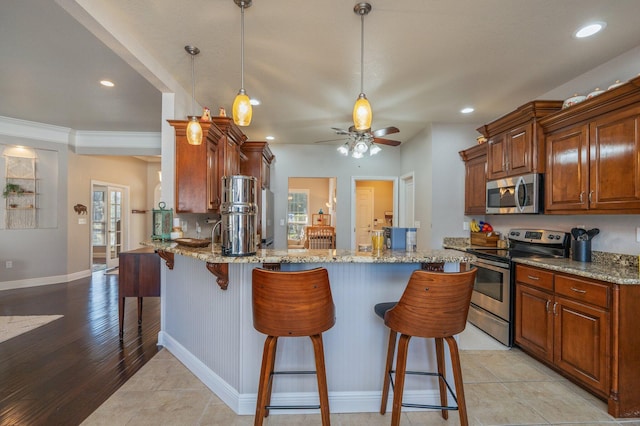 kitchen featuring pendant lighting, light stone counters, a kitchen breakfast bar, appliances with stainless steel finishes, and a peninsula