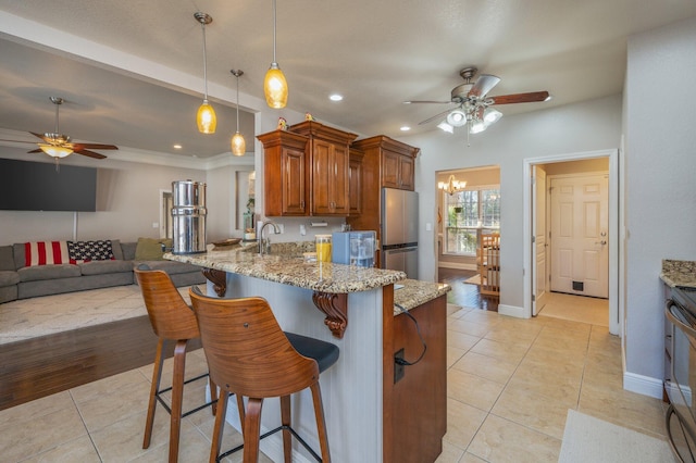 kitchen featuring light stone counters, stainless steel appliances, light tile patterned flooring, and brown cabinetry