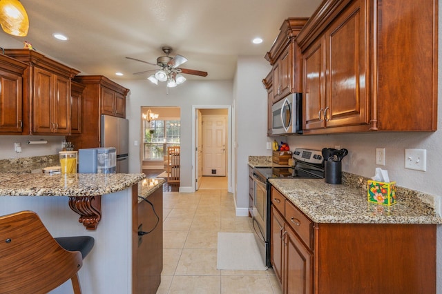 kitchen with a breakfast bar, light tile patterned floors, light stone counters, ceiling fan with notable chandelier, and stainless steel appliances