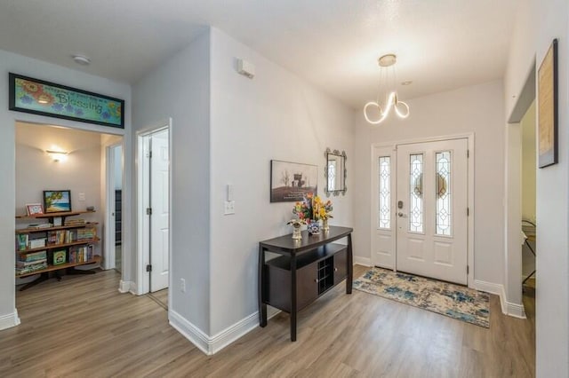 foyer entrance featuring light wood-style flooring, a notable chandelier, and baseboards