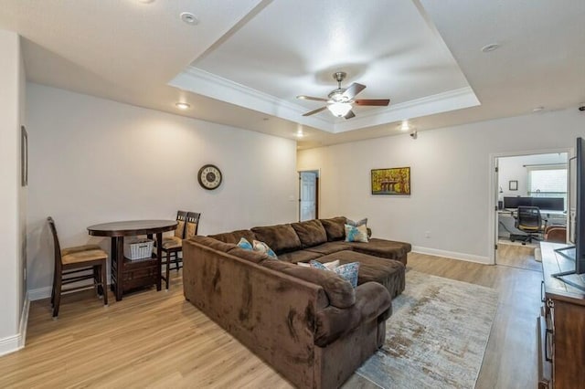 living area featuring light wood-type flooring, a tray ceiling, ornamental molding, and a ceiling fan