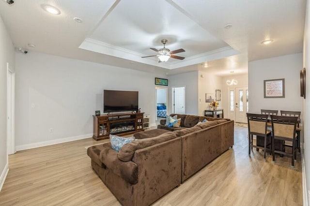 living area with baseboards, a tray ceiling, light wood-style flooring, ceiling fan, and crown molding