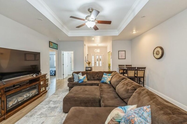 living area with ceiling fan, baseboards, crown molding, and a tray ceiling