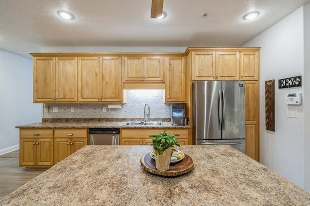 kitchen featuring a sink, light stone counters, wood finished floors, stainless steel appliances, and decorative backsplash