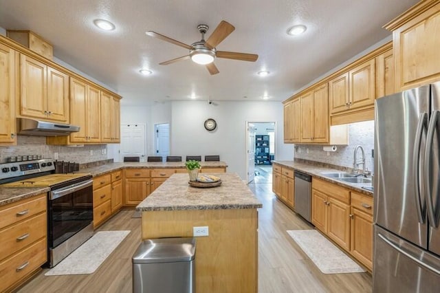 kitchen featuring a kitchen island, under cabinet range hood, appliances with stainless steel finishes, a ceiling fan, and a sink