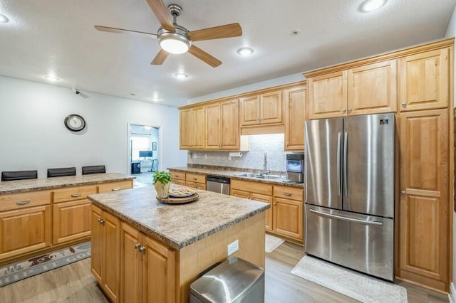 kitchen featuring a kitchen island, ceiling fan, light wood-style flooring, appliances with stainless steel finishes, and a sink