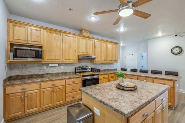 kitchen featuring light wood-style flooring, under cabinet range hood, a kitchen island, tasteful backsplash, and stainless steel appliances