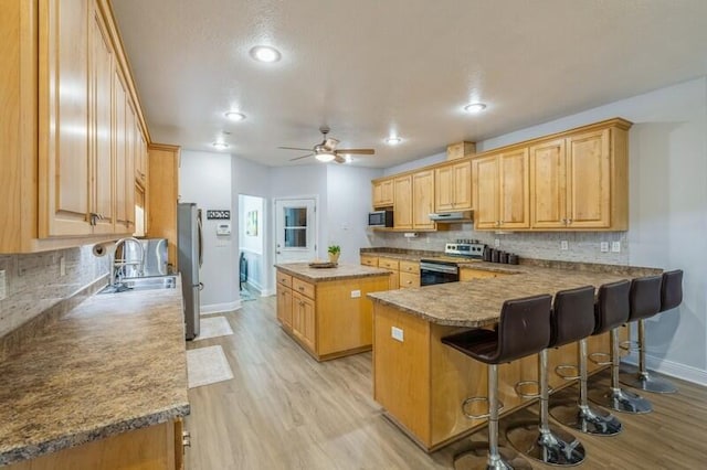 kitchen with light wood-style flooring, a sink, under cabinet range hood, appliances with stainless steel finishes, and a center island