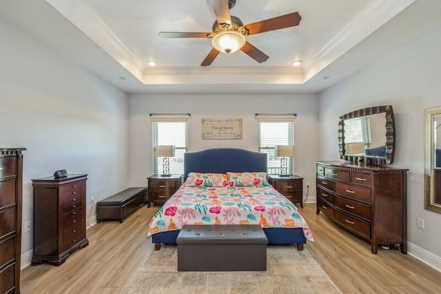 bedroom with a raised ceiling, multiple windows, and light wood finished floors