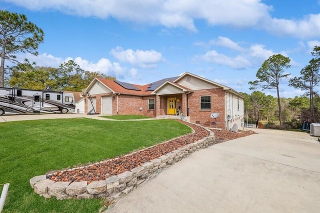 single story home with brick siding, solar panels, an attached garage, a front yard, and driveway