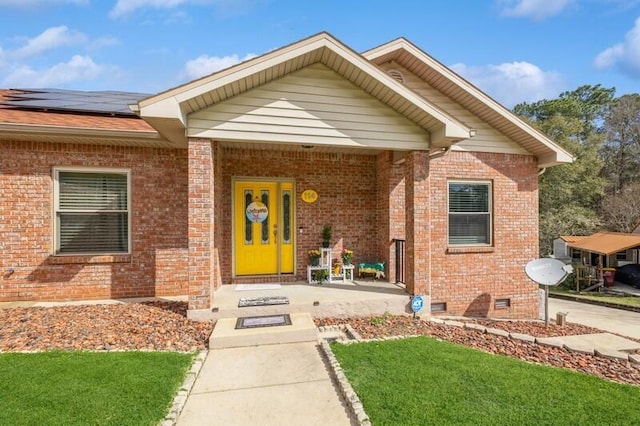 doorway to property featuring solar panels, brick siding, and crawl space