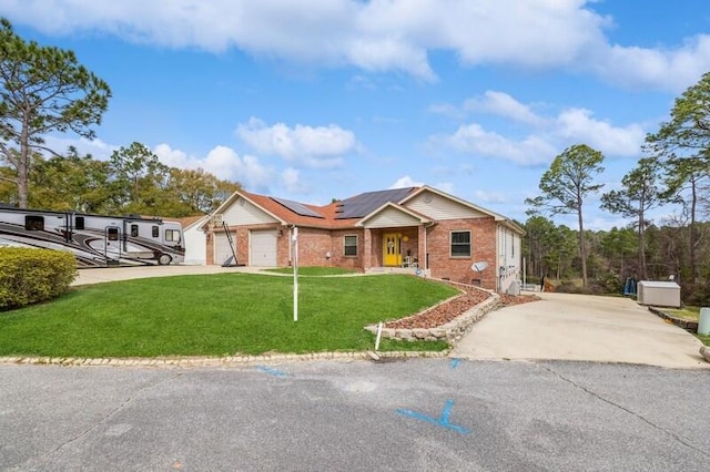 ranch-style home featuring driveway, a front yard, a garage, brick siding, and solar panels