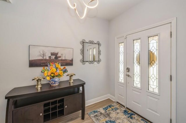 foyer entrance featuring a chandelier, baseboards, and wood finished floors